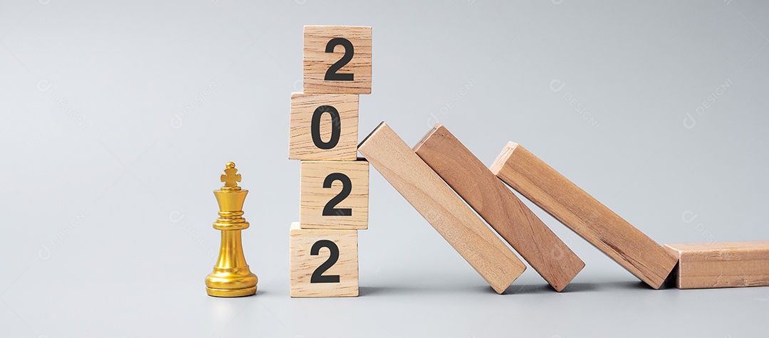 Dominós de madeira caindo contra os blocos de parada de 2022 com figura dourada do Chess King. Conceito de negócios, gerenciamento de riscos, solução, econômico, seguro e ano novo