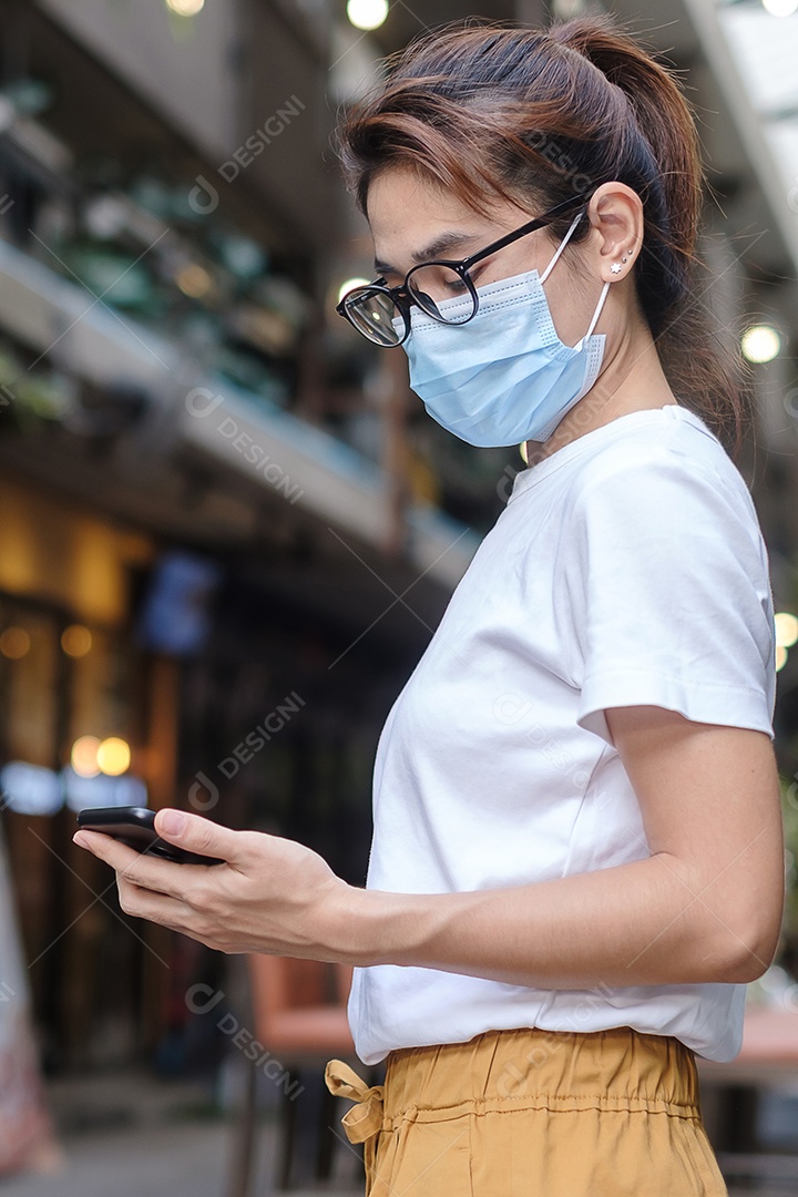 Mulher usando máscara facial médica e usando smartphone durante a caminhada