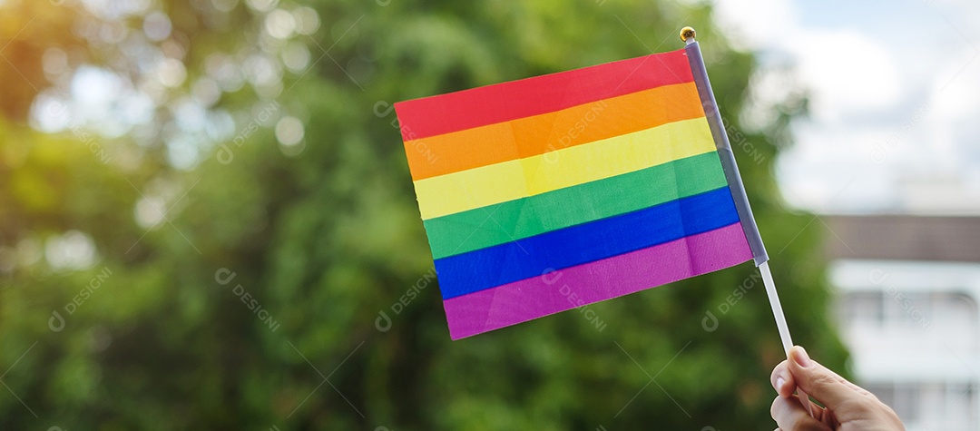 mãos mostrando a bandeira LGBTQ Rainbow no fundo verde da natureza