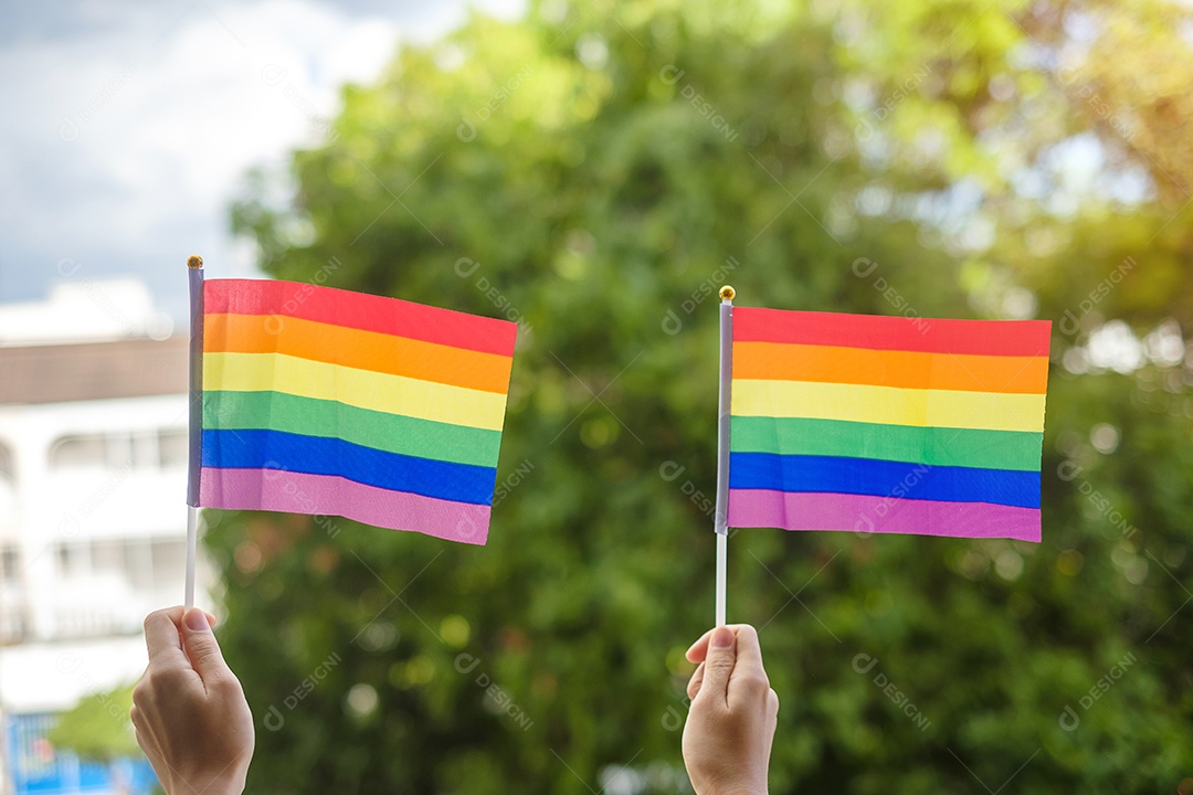 mãos mostrando a bandeira LGBTQ Rainbow no fundo verde da natureza