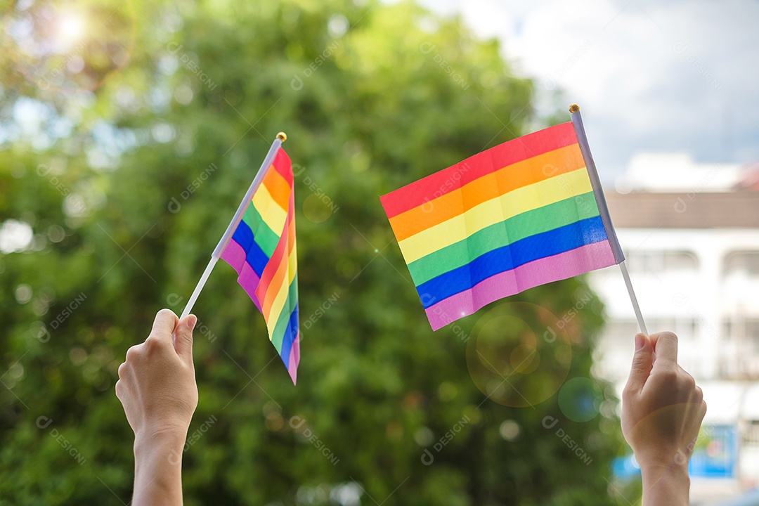 mãos mostrando a bandeira LGBTQ Rainbow no fundo verde da natureza