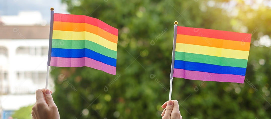 mãos mostrando a bandeira LGBTQ Rainbow no fundo verde da natureza