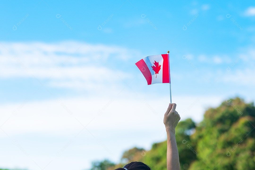 mão segurando a bandeira do Canadá sobre fundo de céu azul