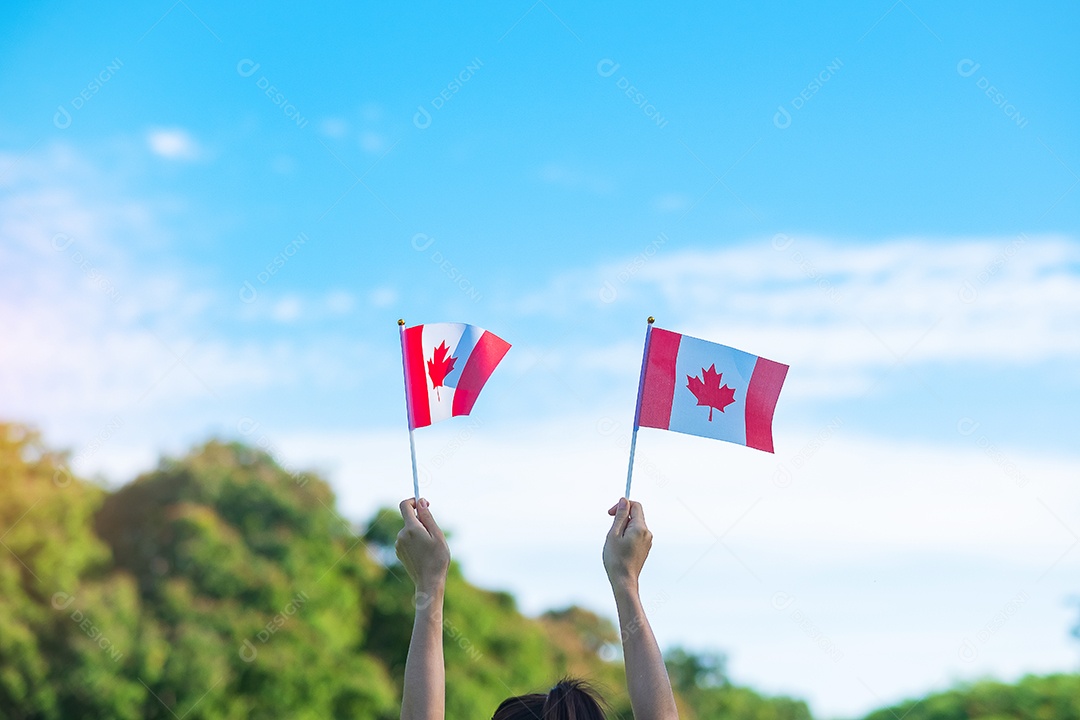 mão segurando a bandeira do Canadá sobre fundo de céu azul