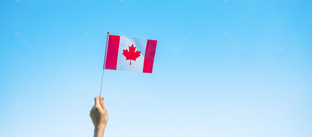 mão segurando a bandeira do Canadá sobre fundo de céu azul.