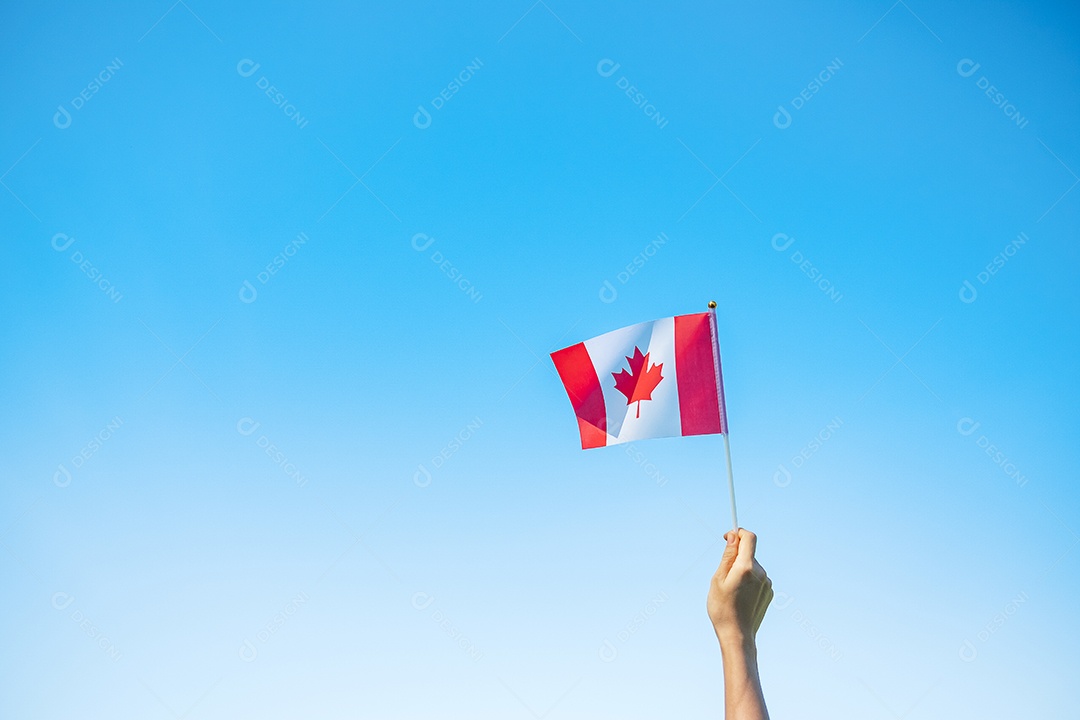 mão segurando a bandeira do Canadá sobre fundo de céu azul.