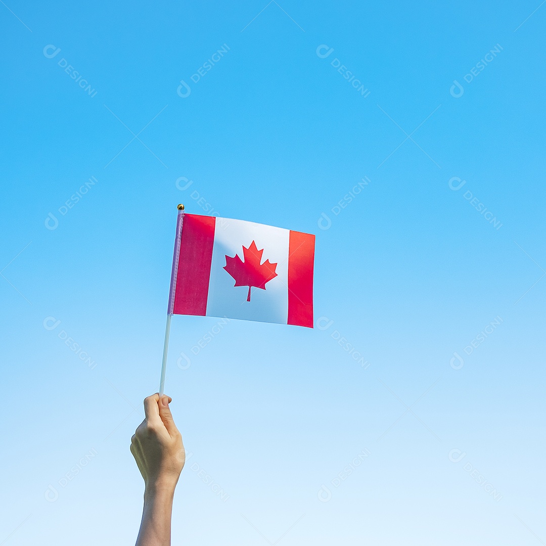 mão segurando a bandeira do Canadá sobre fundo de céu azul.