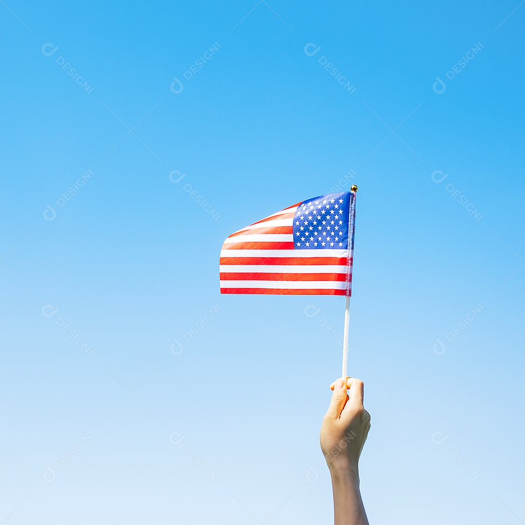 mão segurando a bandeira dos Estados Unidos da América no fundo do céu azul