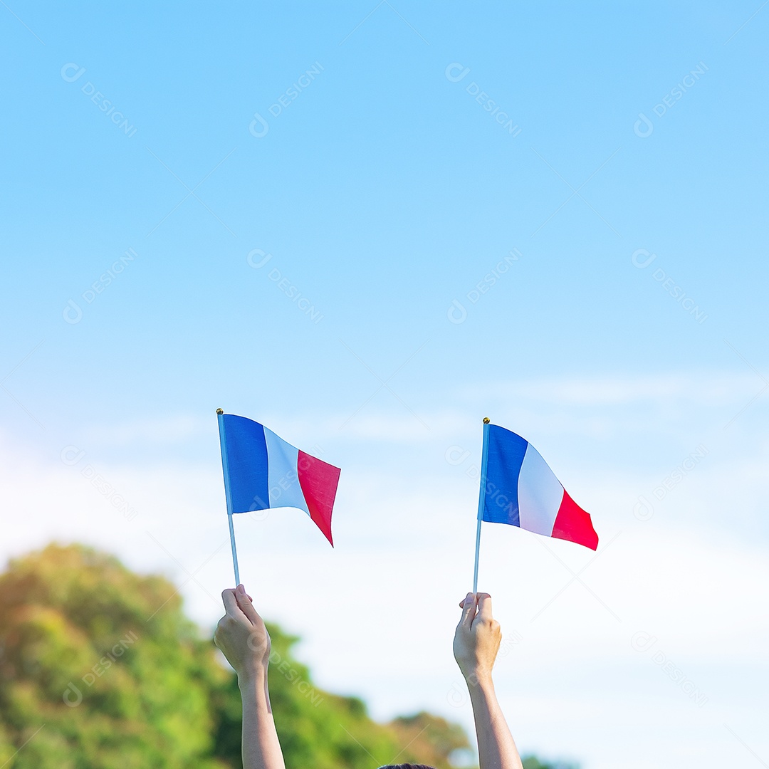 mão segurando a bandeira da França sobre fundo de céu azul.
