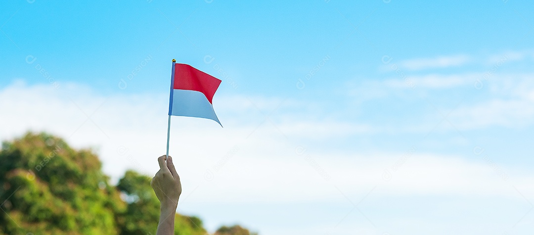 mão segurando a bandeira da Indonésia no fundo do céu azul