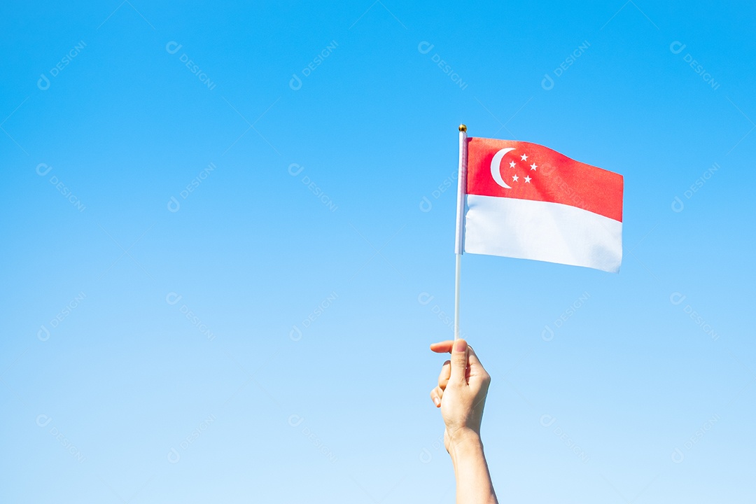 mão segurando a bandeira de Singapura no fundo do céu azul