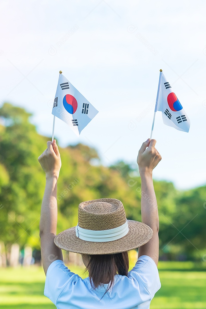 Mão de uma mulher segurando a bandeira da Coreia no fundo da natureza.
