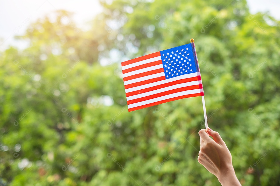 Mão segurando a bandeira dos Estados Unidos da América sobre fundo verde.