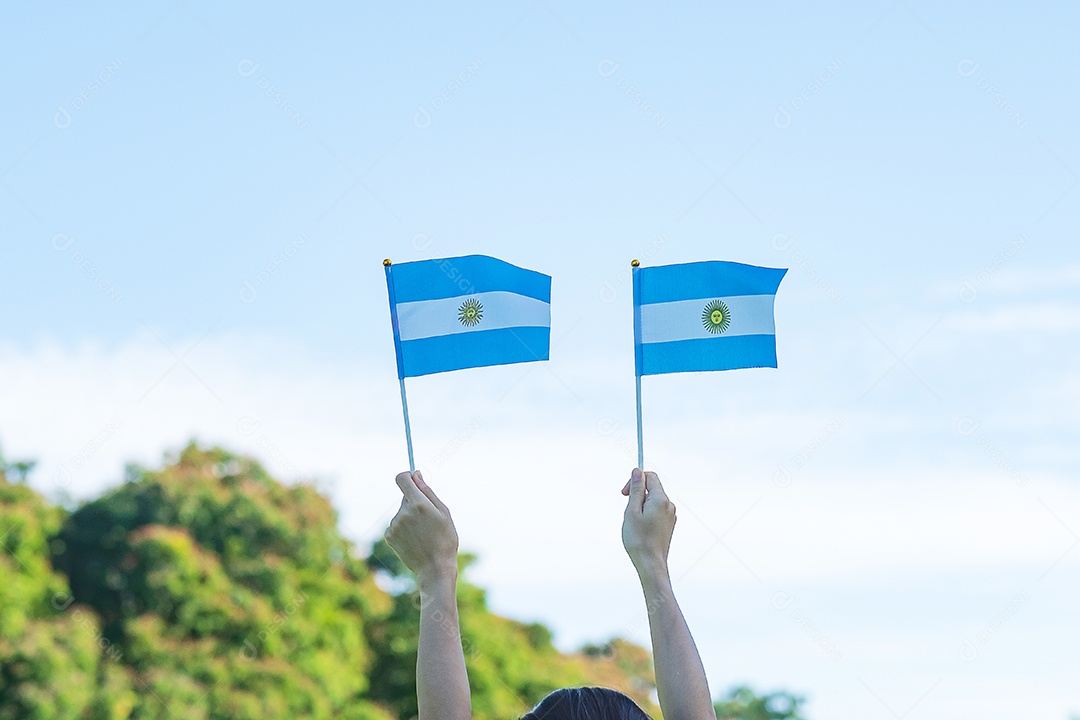 Mão segurando a bandeira da Argentina no fundo da natureza.