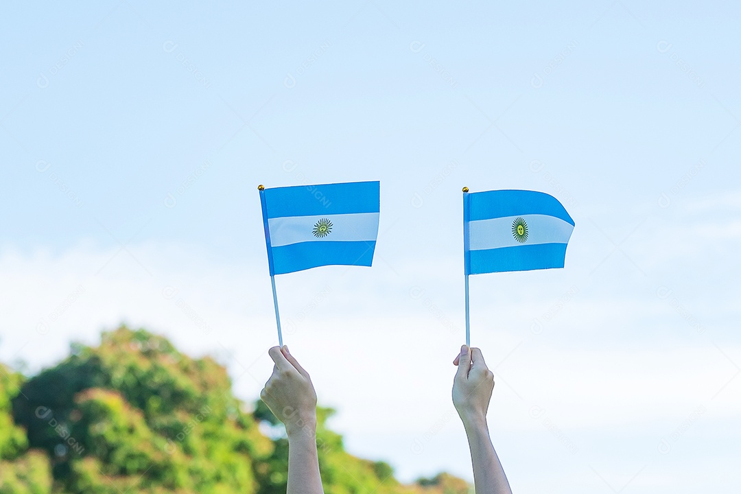 Mão segurando a bandeira da Argentina no fundo da natureza.