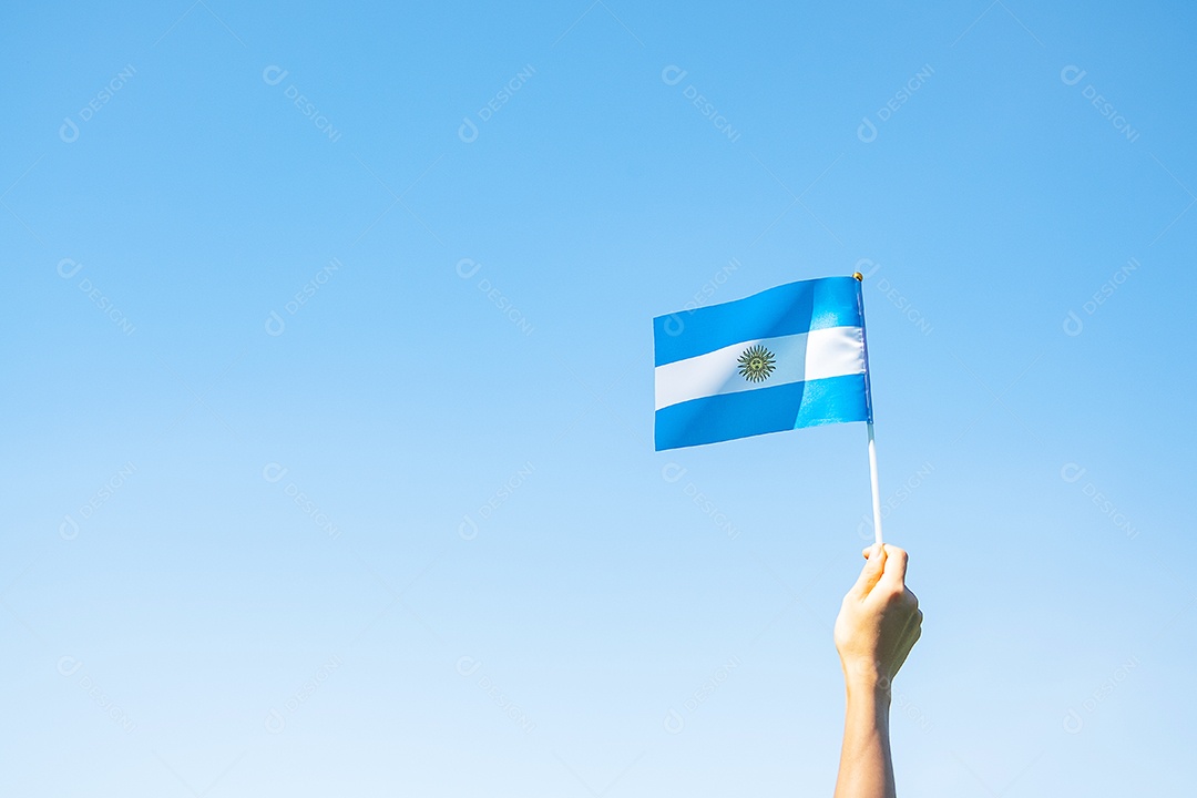 Mão segurando a bandeira da Argentina no fundo da natureza.