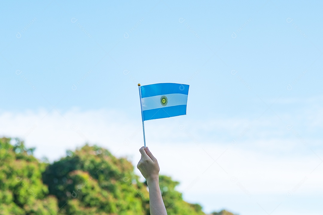 Mão segurando a bandeira da Argentina no fundo da natureza.