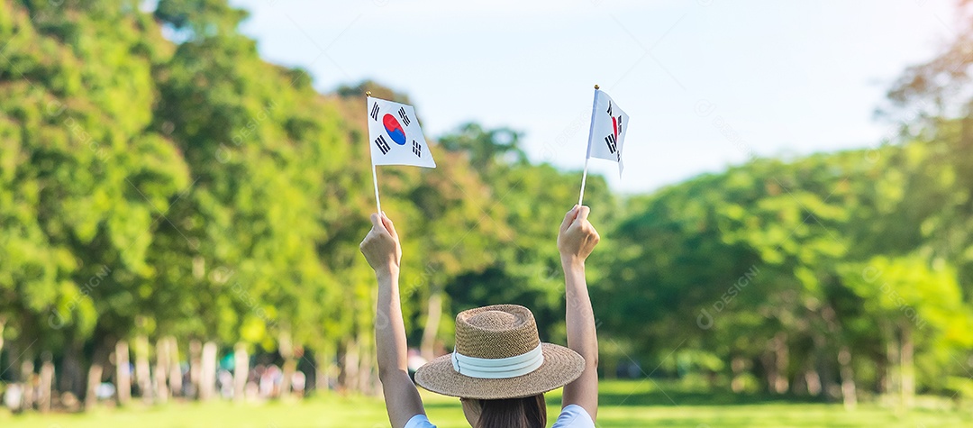 Mão de uma mulher segurando a bandeira da Coreia no fundo da natureza.