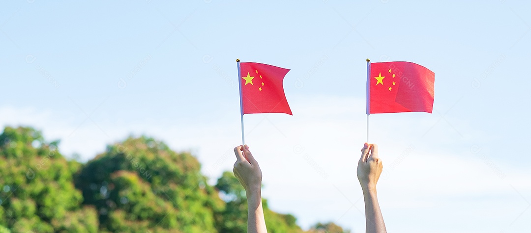 Mão segurando a bandeira da China no fundo do céu azul. Dia Nacional.