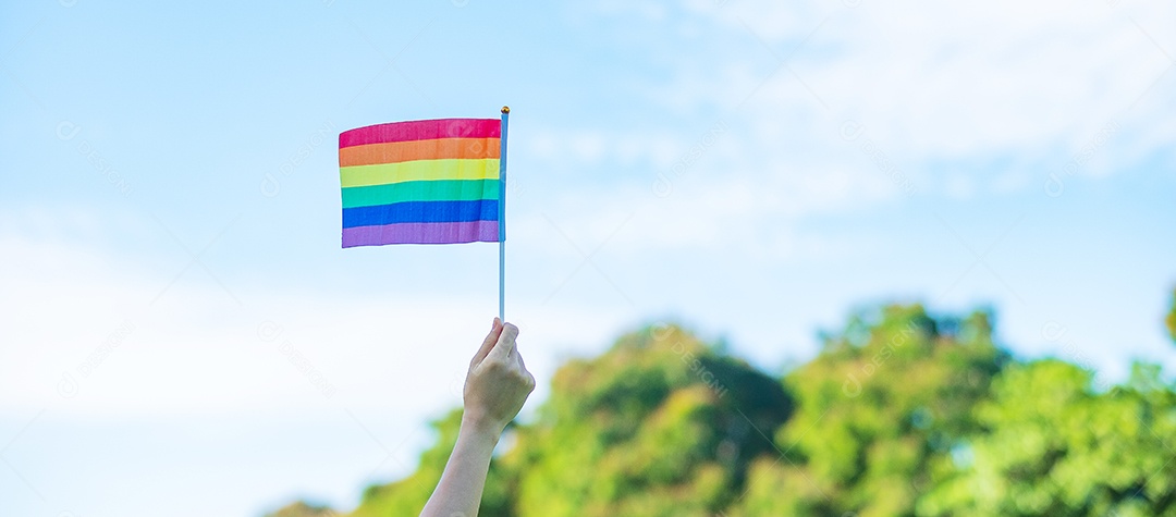 Mãos mostrando a bandeira LGBTQ Arco-íris no fundo da natureza.
