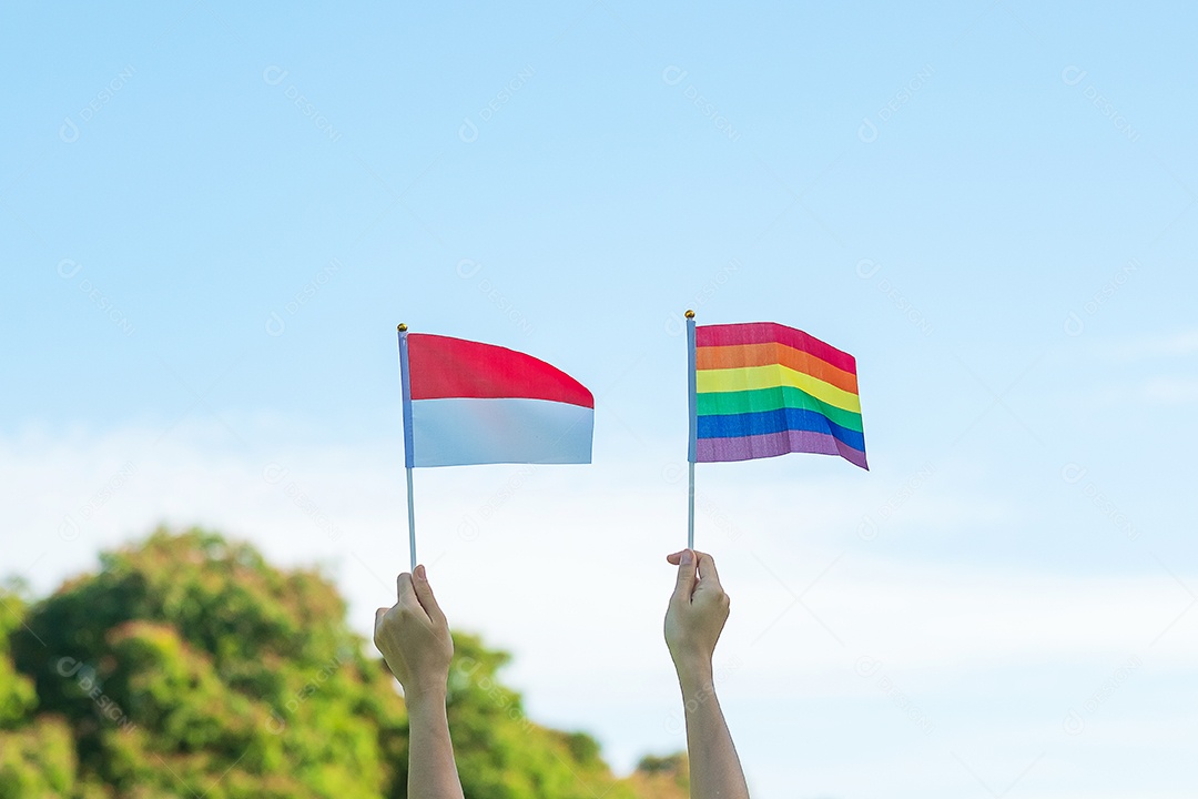 Mãos mostrando LGBTQ Arco-íris e bandeira da Indonésia no fundo da natureza.
