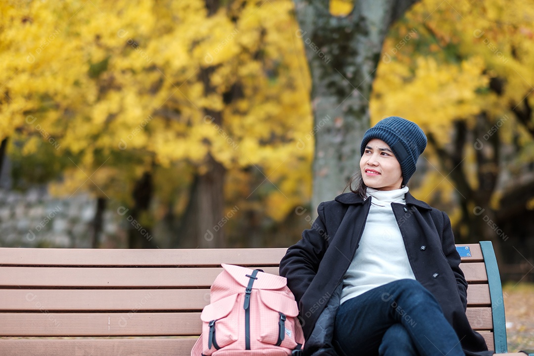 Mulher feliz desfruta no parque ao ar livre na temporada de outono, viajante asiático de casaco e chapéu contra o fundo Yellow Ginkgo Leaves