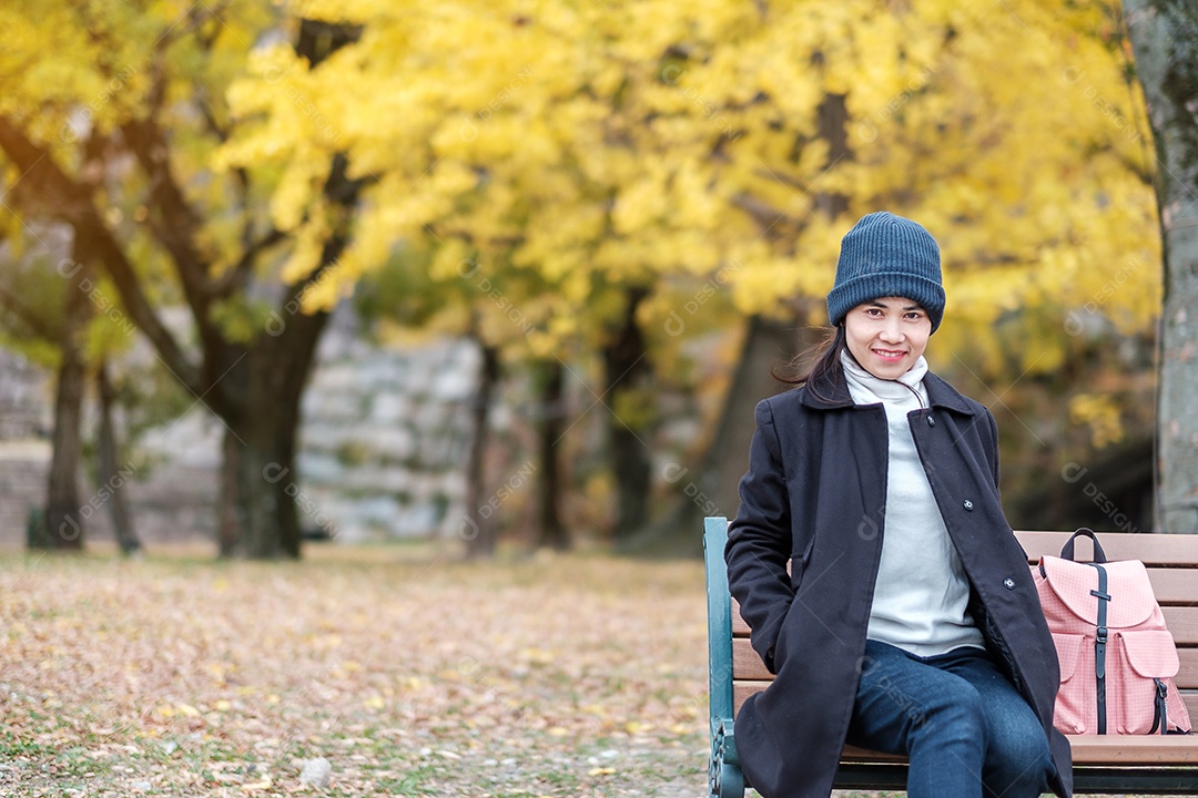 Mulher feliz desfruta no parque ao ar livre na temporada de outono, viajante asiático de casaco e chapéu contra o fundo Yellow Ginkgo Leaves