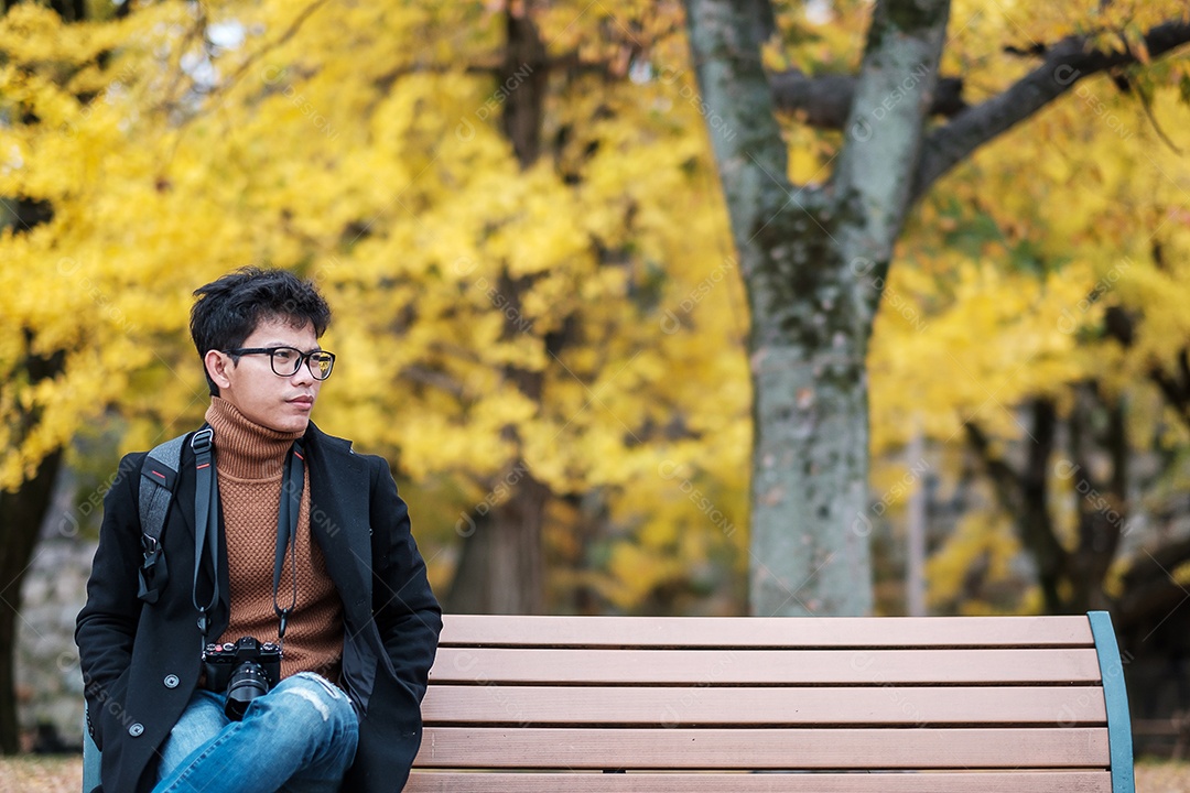 Homem feliz desfruta no parque ao ar livre na temporada de outono, viajante asiático de casaco e câmera contra o fundo Yellow Ginkgo Leaves