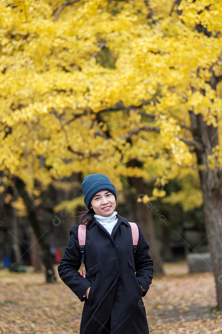 Mulher feliz desfruta no parque ao ar livre na temporada de outono, viajante asiático de casaco e chapéu contra o fundo Yellow Ginkgo Leaves