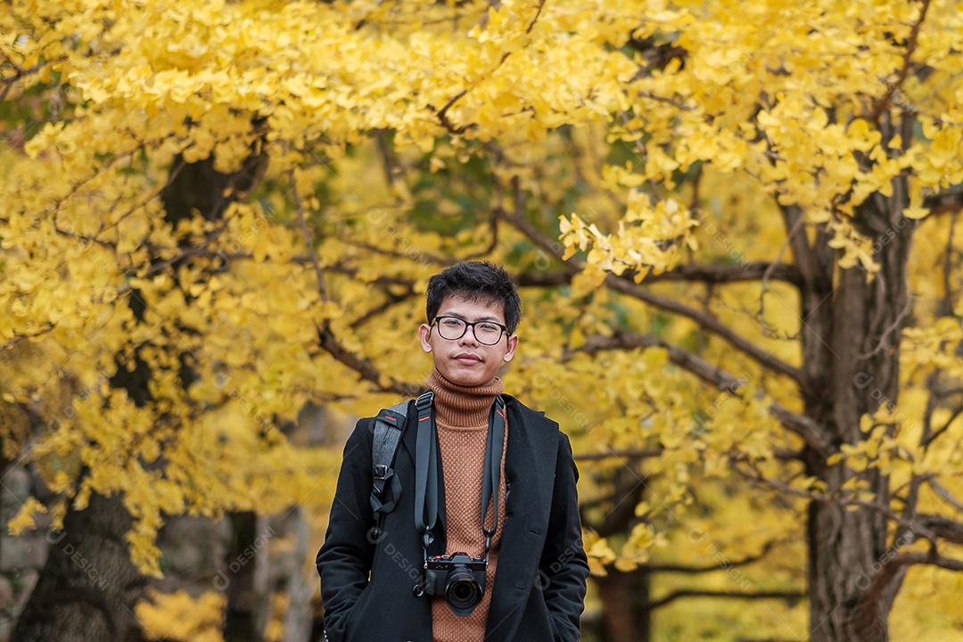 Homem feliz desfruta no parque ao ar livre na temporada de outono, viajante asiático de casaco e câmera contra o fundo Yellow Ginkgo Leaves