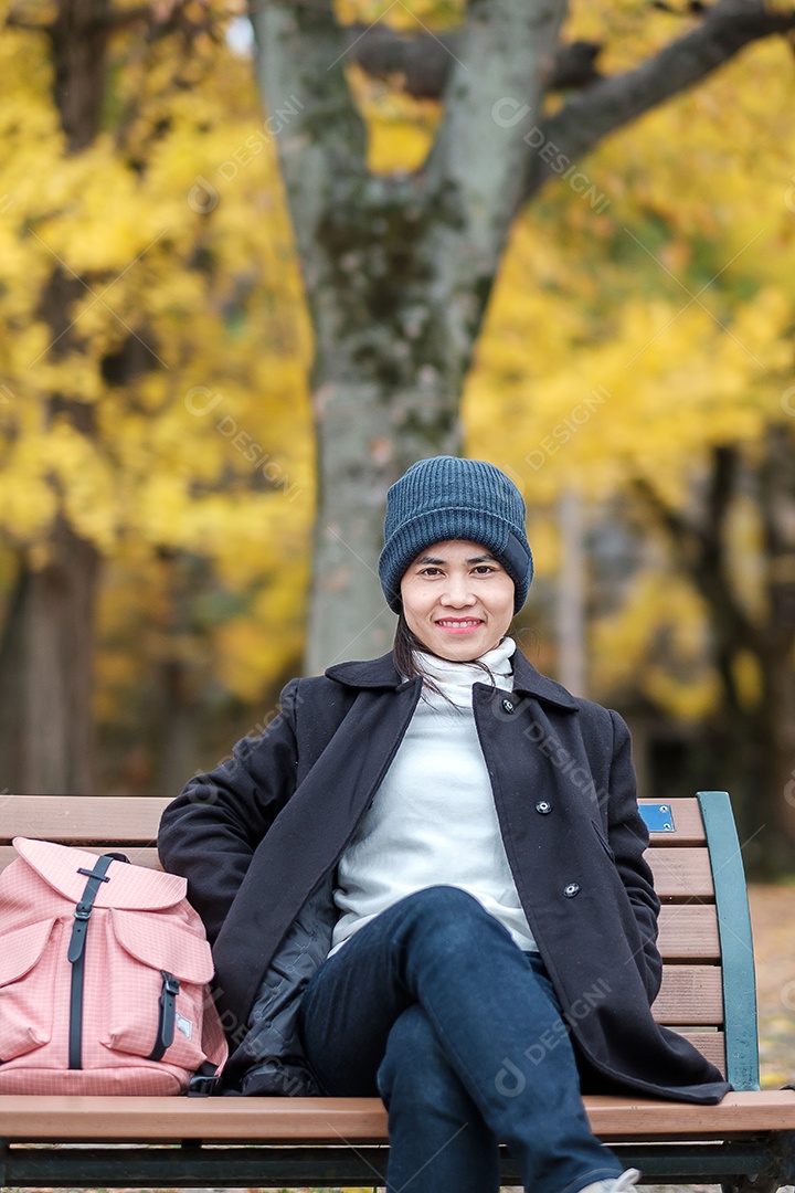 Mulher feliz desfruta no parque ao ar livre na temporada de outono, viajante asiático de casaco e chapéu contra o fundo Yellow Ginkgo Leaves