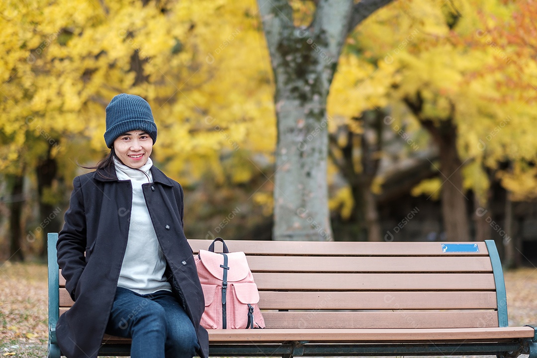 Mulher feliz desfruta no parque ao ar livre na temporada de outono, viajante asiático de casaco e chapéu contra o fundo Yellow Ginkgo Leaves