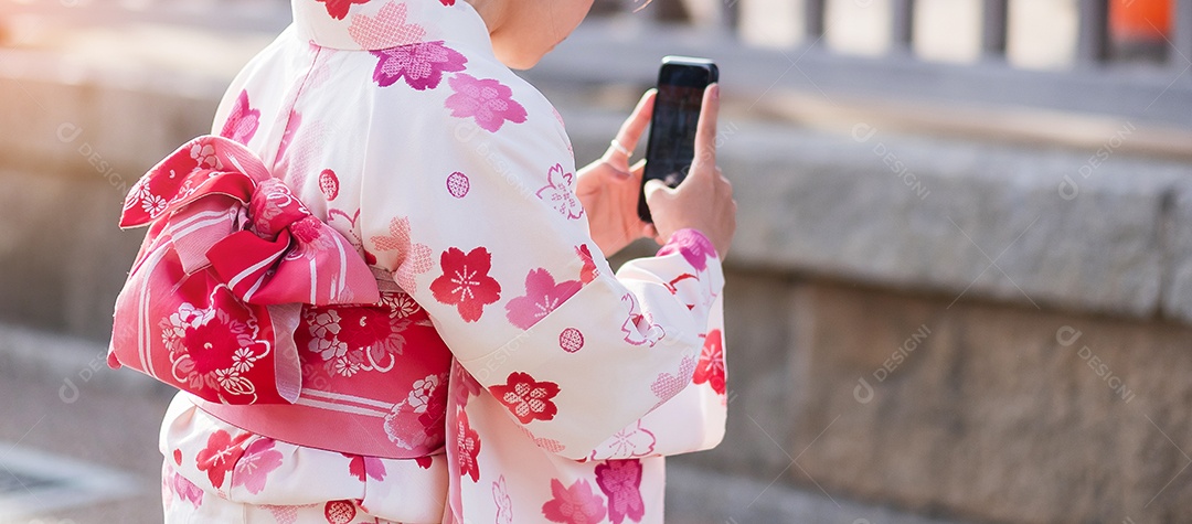 Turista de mulher vestindo quimono tira uma foto por smartphone móvel no templo Kiyomizu dera, Kyoto, Japão. Menina asiática em roupas tradicionais japonesas na temporada de folhagem de outono