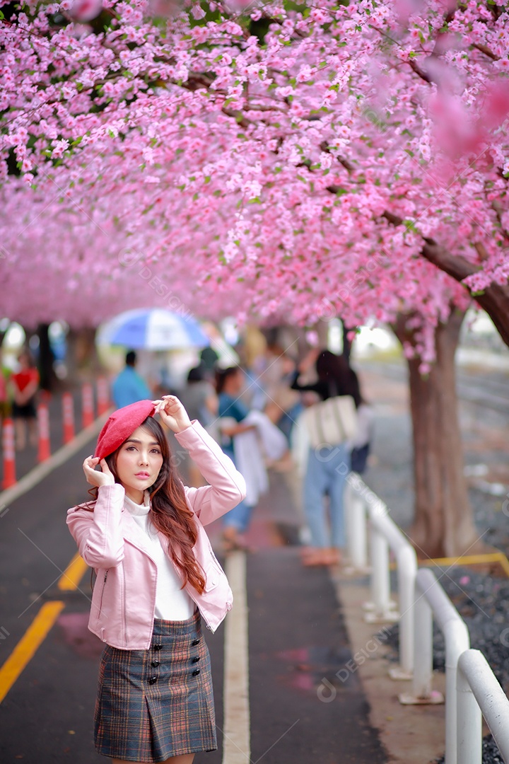 Uma mulher viajante hipster passear usa um chapéu vermelho com uma bela árvore de flores de cerejeira sakura desabrochando na cor rosa no parque em um dia de primavera.