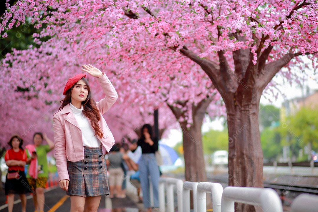 Uma mulher viajante hipster passear usa um chapéu vermelho com uma bela árvore de flores de cerejeira sakura desabrochando na cor rosa no parque em um dia de primavera.