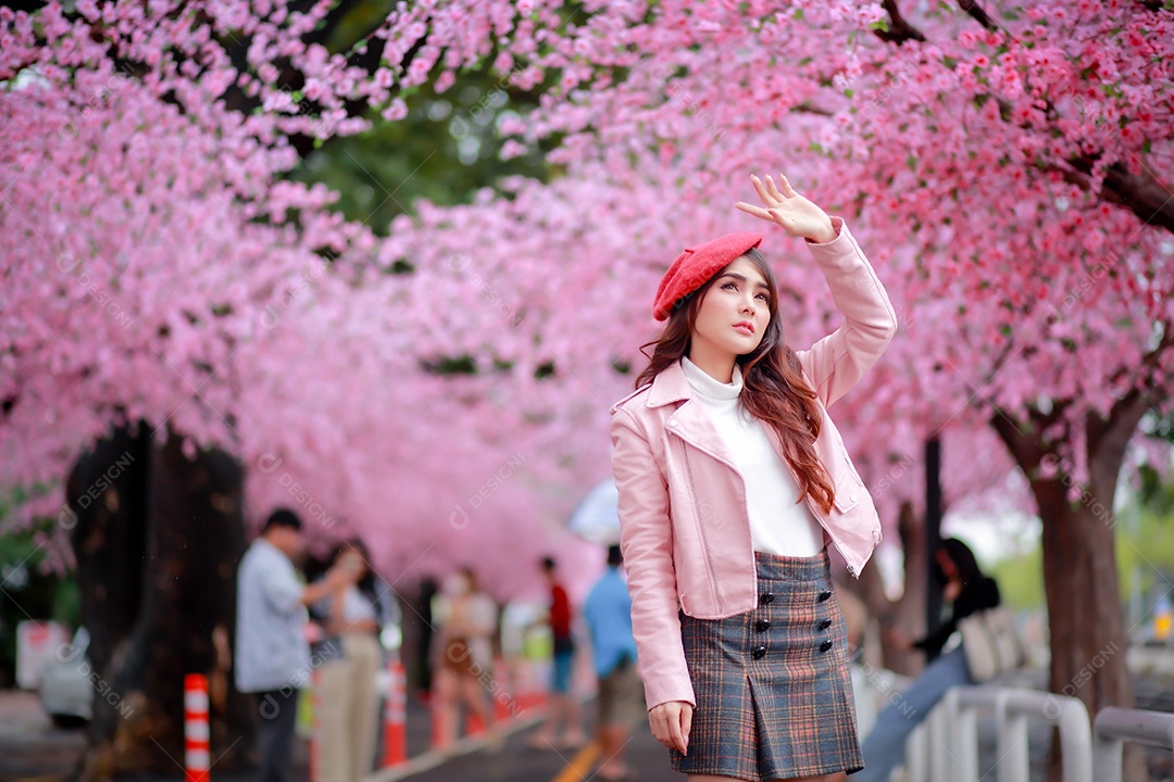 Uma mulher viajante hipster passear usa um chapéu vermelho com uma bela árvore de flores de cerejeira sakura desabrochando na cor rosa no parque em um dia de primavera.