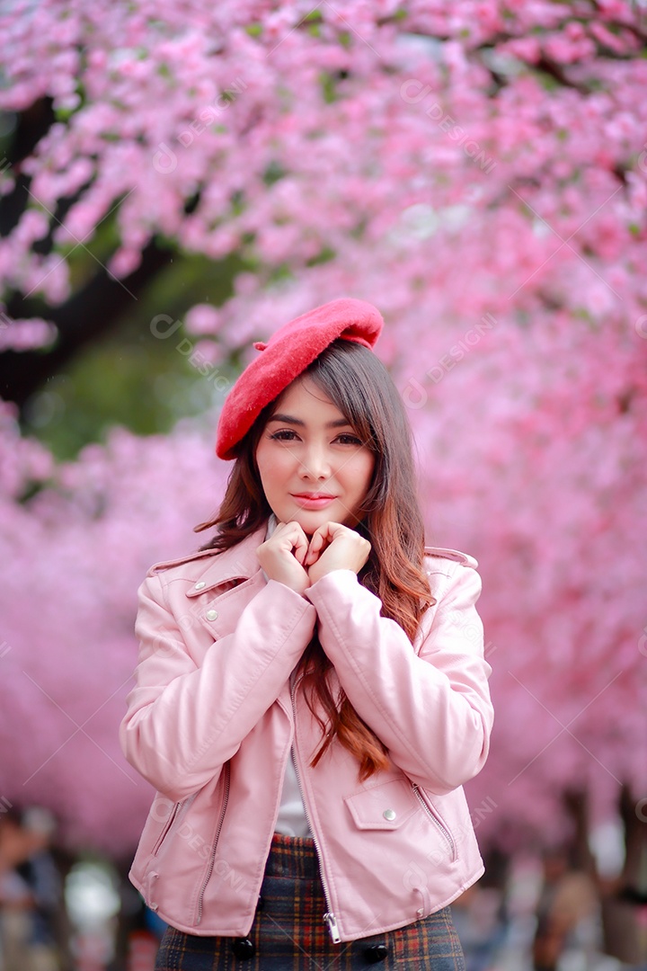 Uma mulher viajante hipster passear usa um chapéu vermelho com uma bela árvore de flores de cerejeira sakura desabrochando na cor rosa no parque em um dia de primavera.