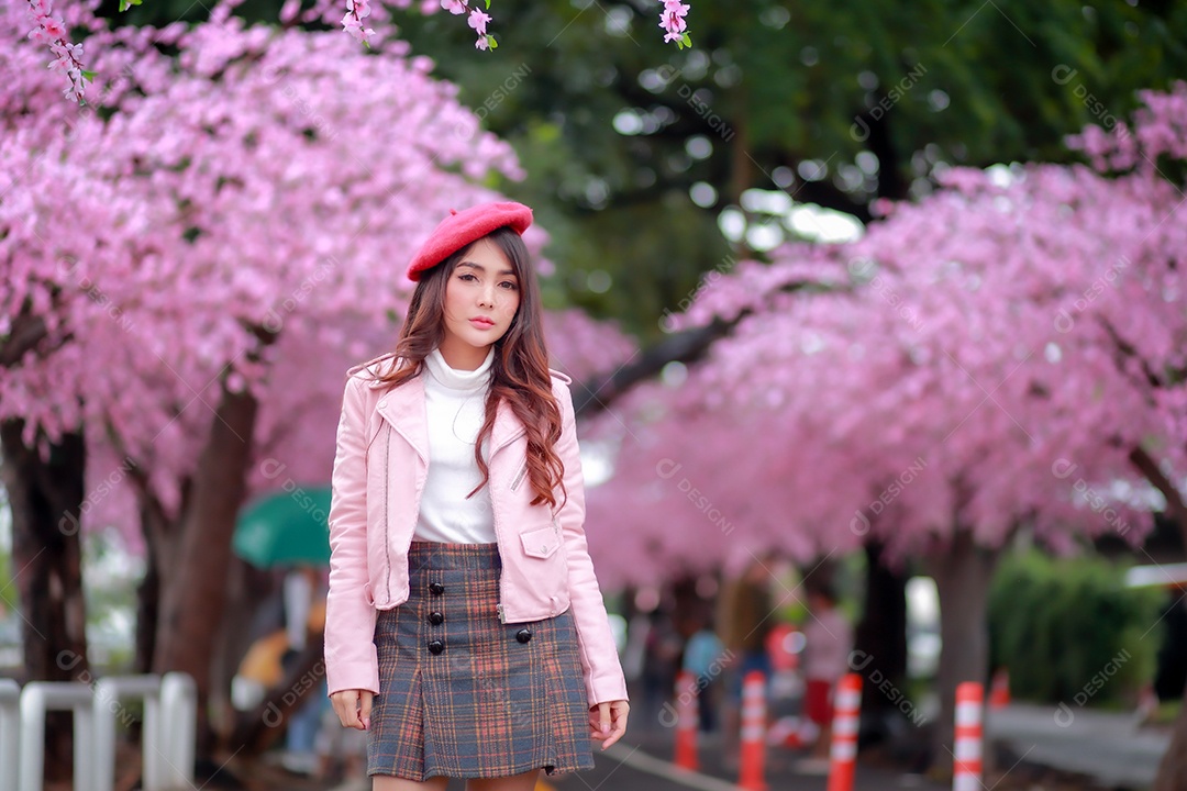 Uma mulher viajante hipster passear usa um chapéu vermelho com uma bela árvore de flores de cerejeira sakura desabrochando na cor rosa no parque em um dia de primavera.