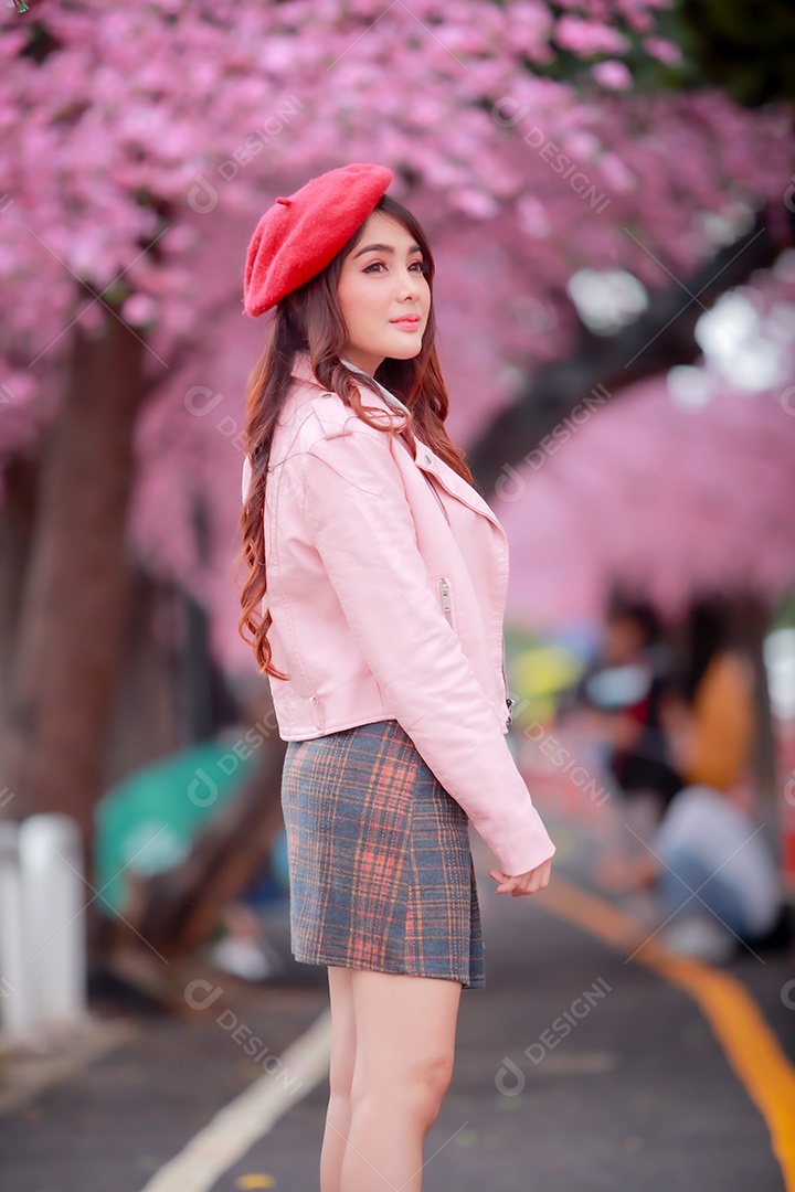 Uma mulher viajante hipster passear usa um chapéu vermelho com uma bela árvore de flores de cerejeira sakura desabrochando na cor rosa no parque em um dia de primavera.