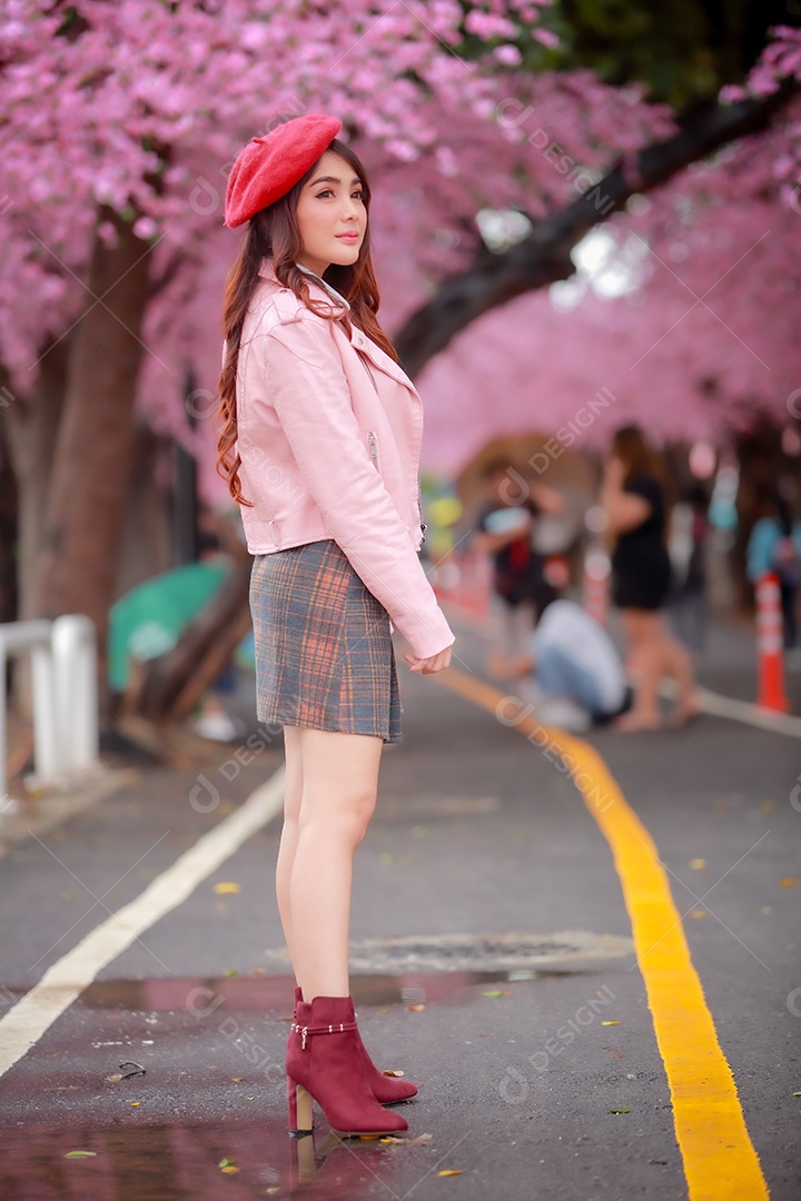 Uma mulher viajante hipster passear usa um chapéu vermelho com uma bela árvore de flores de cerejeira sakura desabrochando na cor rosa no parque em um dia de primavera.