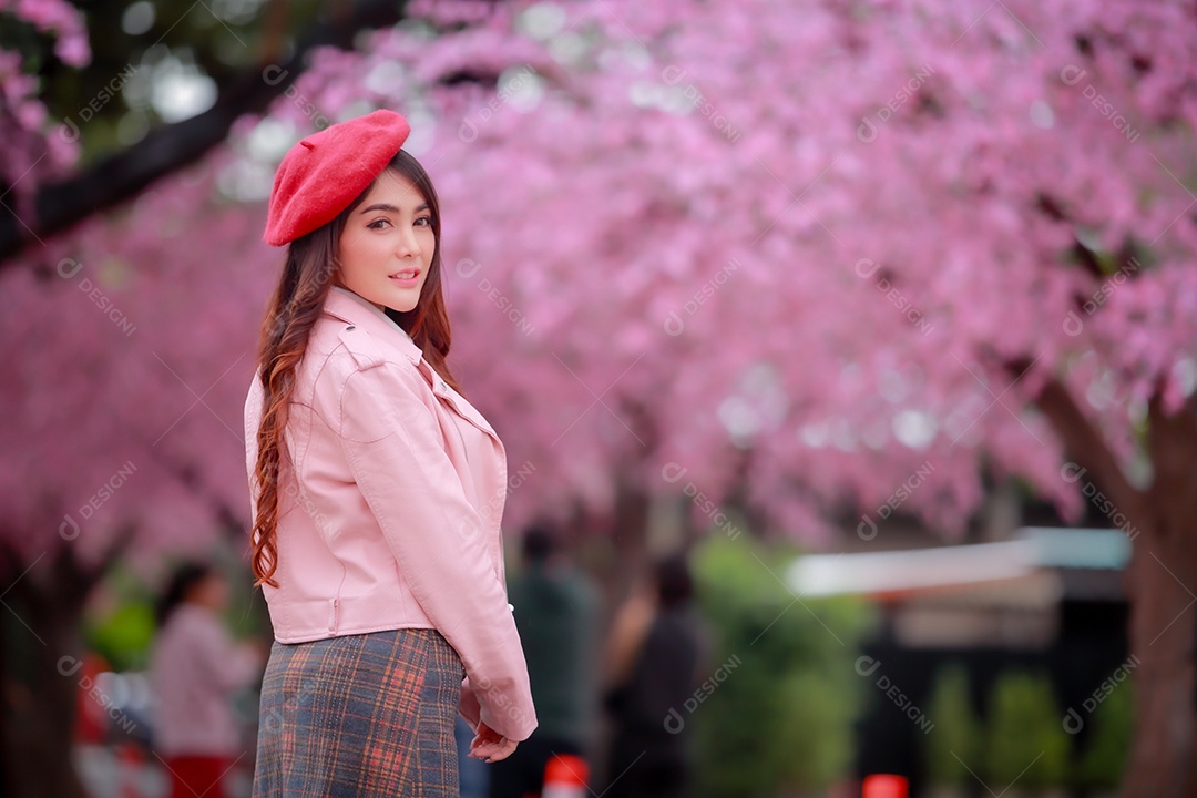 Uma mulher viajante hipster passear usa um chapéu vermelho com uma bela árvore de flores de cerejeira sakura desabrochando na cor rosa no parque em um dia de primavera.