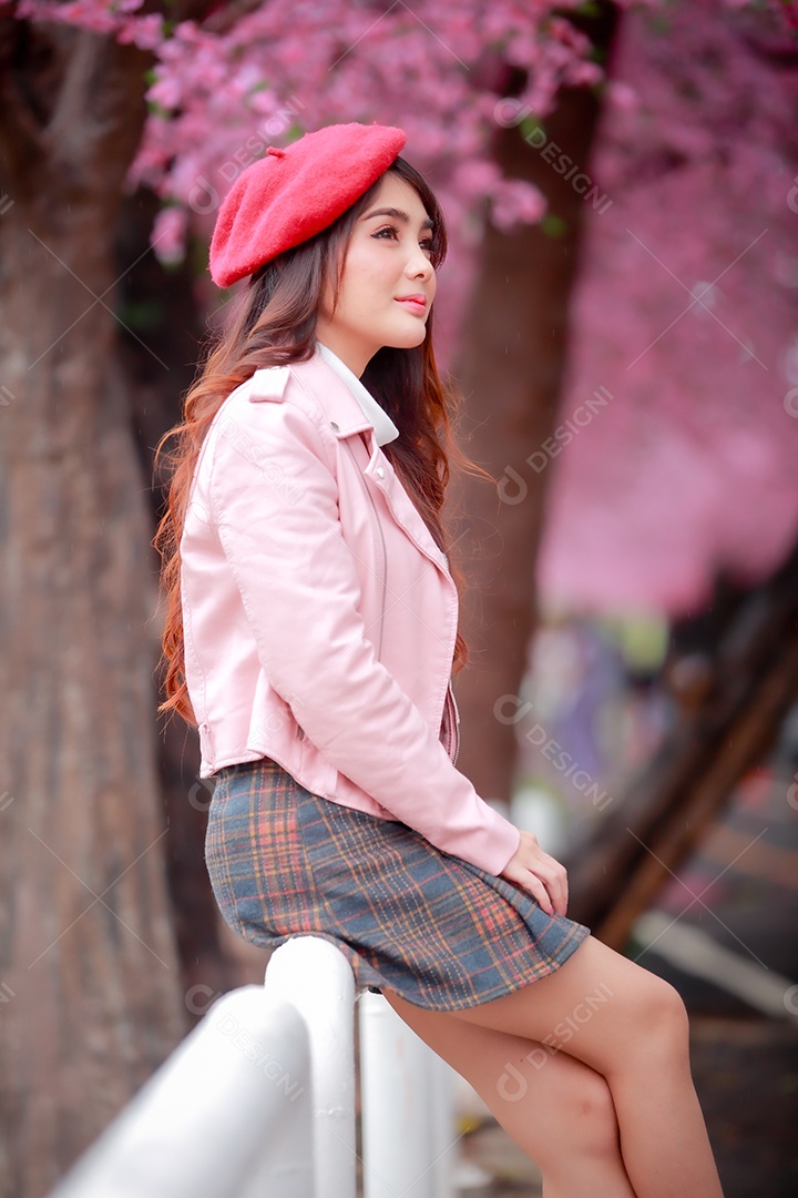 Uma mulher viajante hipster passear usa um chapéu vermelho e um vestido de couro liso com uma bela árvore de flores de cerejeira sakura desabrochando na cor rosa no parque em um dia de primavera.