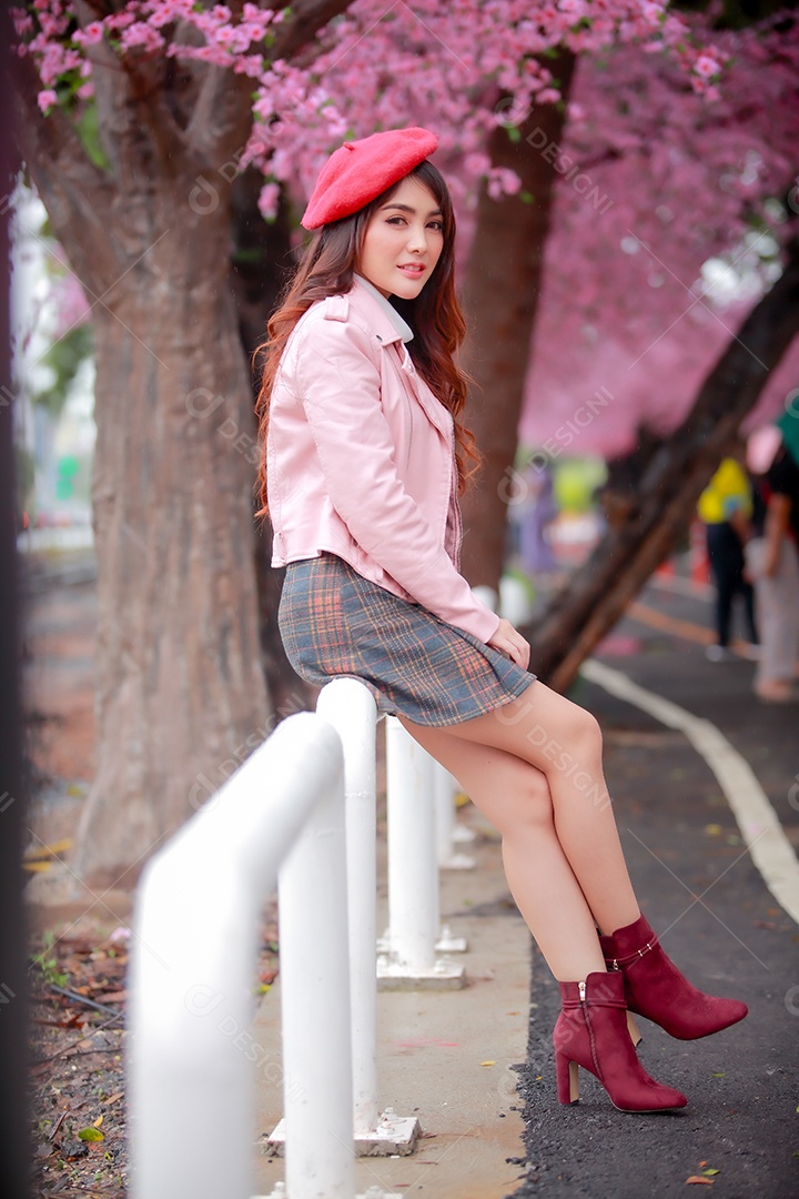 Uma mulher viajante hipster passear usa um chapéu vermelho e um vestido de couro liso com uma bela árvore de flores de cerejeira sakura desabrochando na cor rosa no parque em um dia de primavera.