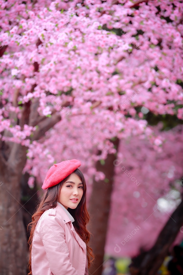 Uma mulher viajante hipster passear usa um chapéu vermelho e um vestido de couro liso com uma bela árvore de flores de cerejeira sakura desabrochando na cor rosa no parque em um dia de primavera.