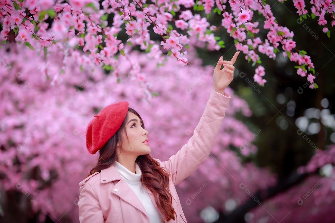 Uma mulher viajante hipster passear usa um chapéu vermelho e um vestido de couro liso com uma bela árvore de flores de cerejeira sakura desabrochando na cor rosa no parque em um dia de primavera.