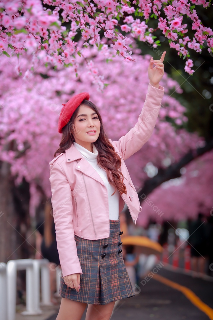 Uma mulher viajante hipster passear usa um chapéu vermelho e um vestido de couro liso com uma bela árvore de flores de cerejeira sakura desabrochando na cor rosa no parque em um dia de primavera.