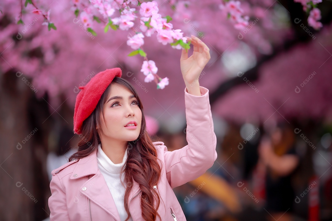 Uma mulher viajante hipster passear usa um chapéu vermelho e um vestido de couro liso com uma bela árvore de flores de cerejeira sakura desabrochando na cor rosa no parque em um dia de primavera.