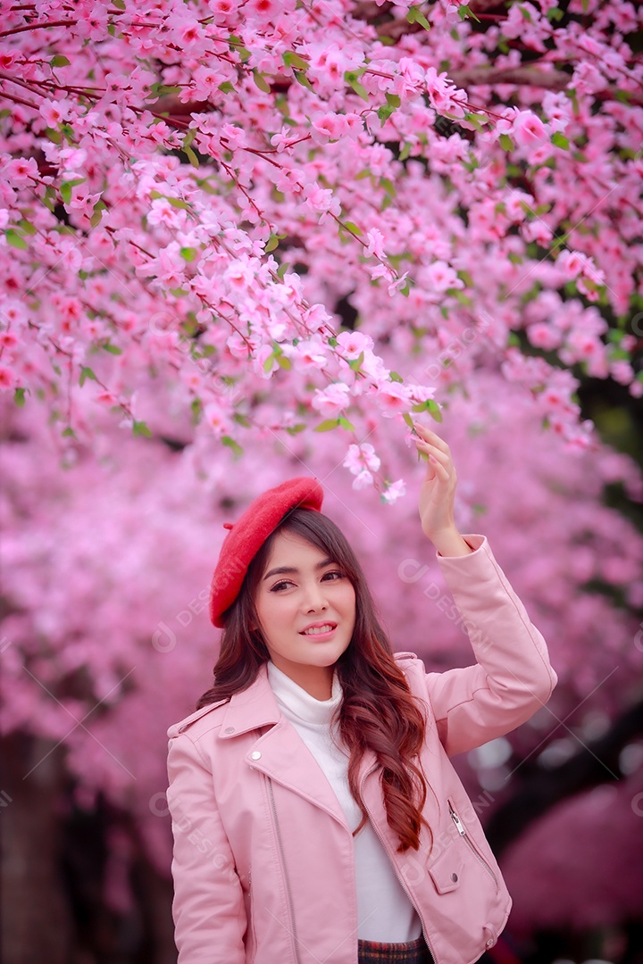 Uma mulher viajante hipster passear usa um chapéu vermelho e um vestido de couro liso com uma bela árvore de flores de cerejeira sakura desabrochando na cor rosa no parque em um dia de primavera.