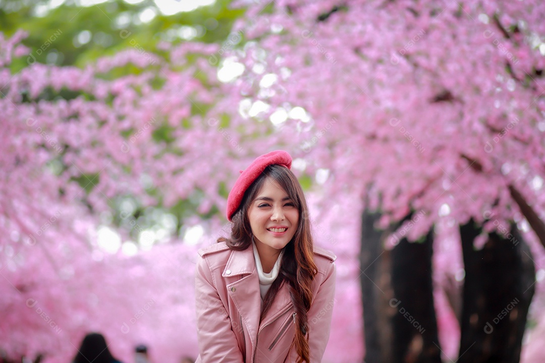 Uma mulher viajante hipster passear usa um chapéu vermelho e um vestido de couro liso com uma bela árvore de flores de cerejeira sakura desabrochando na cor rosa no parque em um dia de primavera.