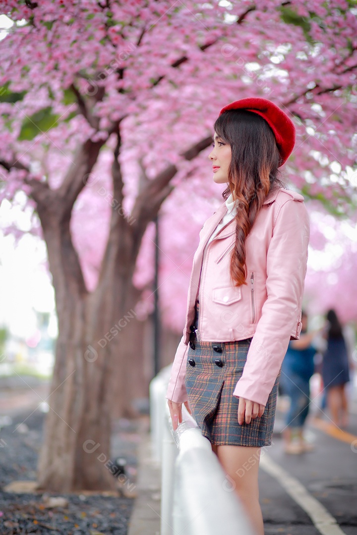 Uma mulher viajante hipster passear usa um chapéu vermelho e um vestido de couro liso com uma bela árvore de flores de cerejeira sakura desabrochando na cor rosa no parque em um dia de primavera.